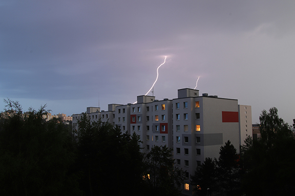 Two lightning strikes hitting the rooftop of a residential apartment building at dusk. Most facilities