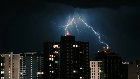 Bright lightning bolt striking the top of a high-rise apartment building against a dark night sky.