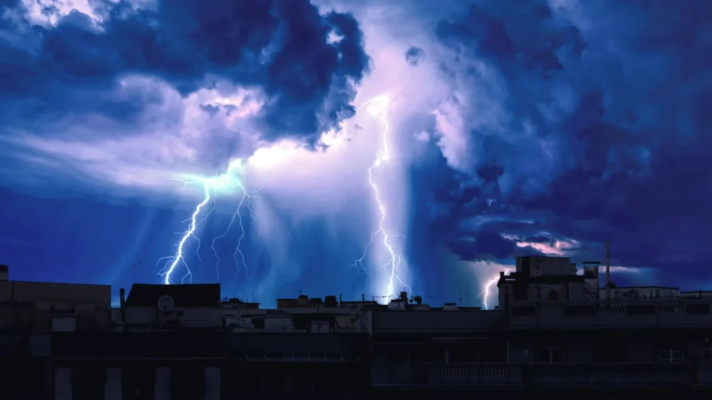 Lightning over a city rooftop skyline under a dramatic blue storm sky.