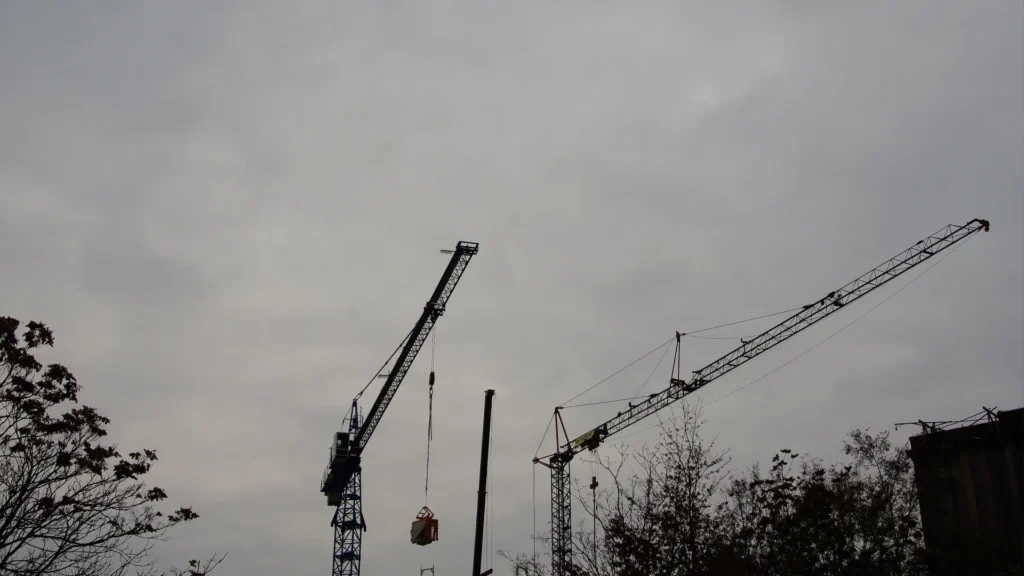 Two construction cranes silhouetted against an overcast grey sky.